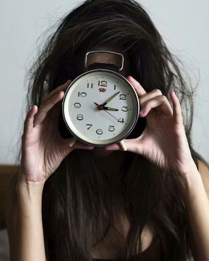 A woman holding an alarm clock in front of her face