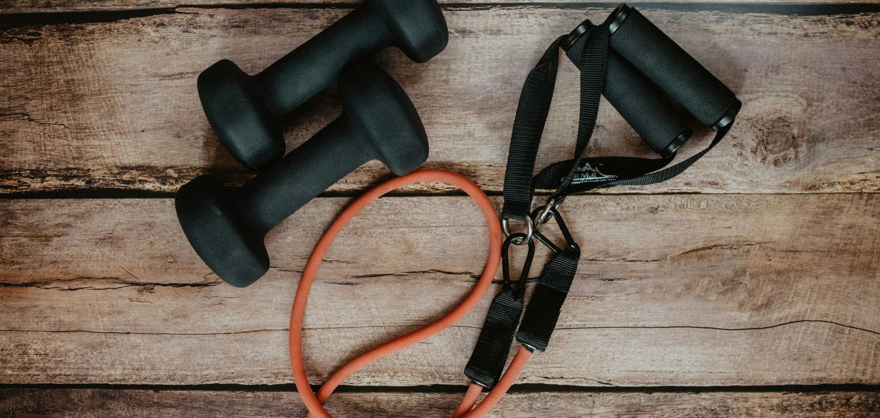 Two dumbbells and a resistance band on a wooden floor