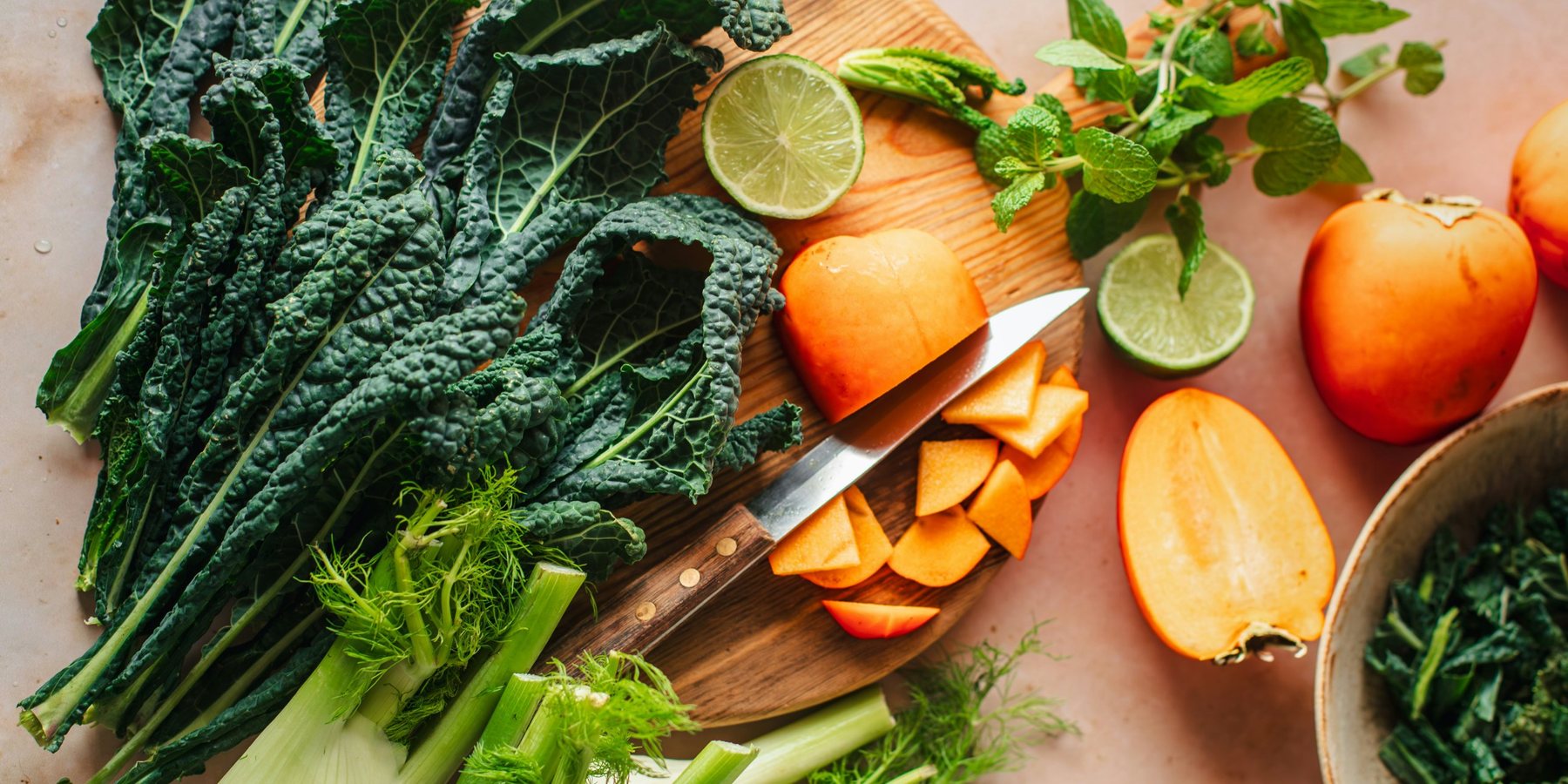 Lacinato kale, fennel, persimmons, lime and mint on a wooden cutting board