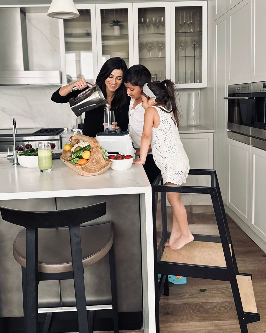 Dr. K making a green smoothie with her two children at the kitchen island, with fresh vegetables, spinach and strawberries on the counter